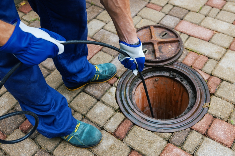 a person holding a hose to a sewer hole
